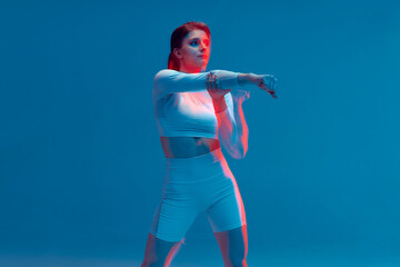 Beautiful girl in white tracksuit on blue background. Hand strike. Isolated fitness model in studio...