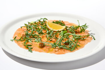 Salmon carpaccio with arugula on white background in summer day. Fish appetizer - salmon carpaccio in fine dining with shadows. Elegant carpaccio of raw salmon and sauce. Italian food. Aesthetic menu.