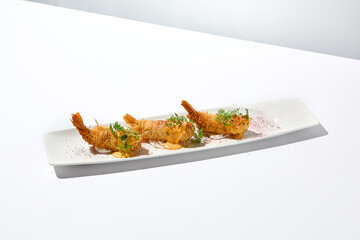 Traditional greek appetizer - kataifi wrapped shrimps on white plate. Crispy shrimp in kataifi crust in summer day. Shrimp appetizer fried in kataifi dough. Crispy prawns in modern style.