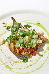 Baked eggplant with cheese on white table with harsh shadows. Aesthetic italian food - baked aubergine on white plate. Stuffed eggplant in minimal style. Stuffed aubergine in vegan menu.