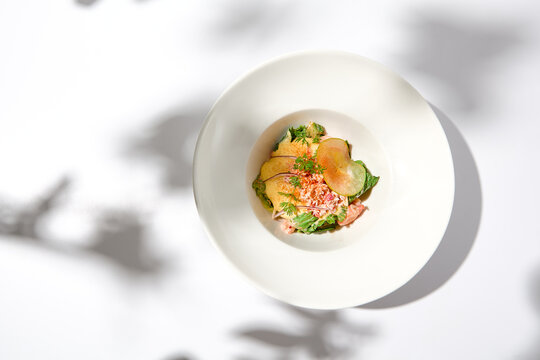Elegant salad with crab meat, espuma sauce and lettuce on white table with harsh shadows. Green salad with crab and creamy sauce in summer menu. Aesthetic food. Seafood appetizer.