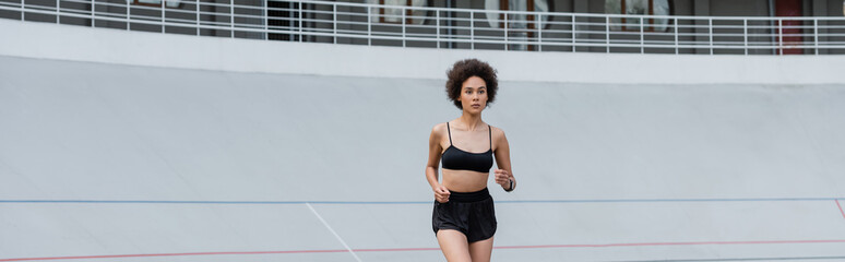 Fototapeta na wymiar young african american woman in black sportswear jogging on stadium, banner.