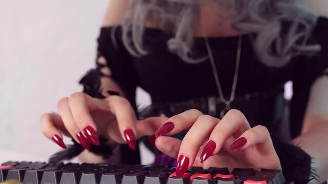 Beautiful young witch in a nice black dress, wearing a witch's hat, sits at the computer typing on the keyboard, working from home for halloween, enjoying it and smiles