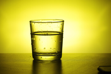 A glass with water at yellow background	