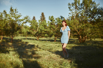 Naklejka na ściany i meble Young beautiful woman walking alone in the forest in blue dress. Enjoying sun and fresh air.