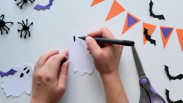 Paper art creation for Halloween - hands drawing the face of a white paper ghost