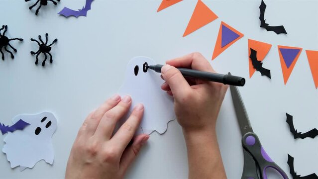 Paper art creation for Halloween - hands drawing the face of a white paper ghost
