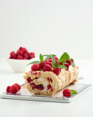Baked meringue roll with cream and fresh red raspberry, white background