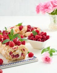 Baked meringue roll with cream and fresh red raspberry on a white board