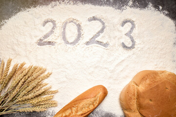 Number 2023 with ears of wheat and loaves of bread on flour. New Year