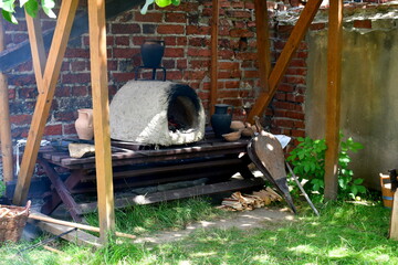 A close up on a medieval oven made out of clay and mud with some equipment usef for firing it up seen nearby under a small cloth laying on a wooden frame in the middle of a public park in Poland