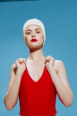 An haughty female model in a bathing cap lifts the straps of a swimsuit, looking at the camera....