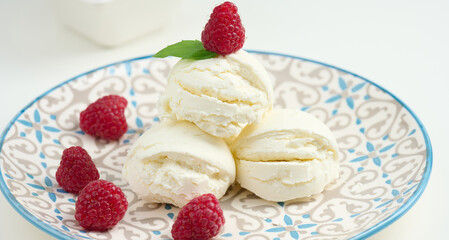 Vanilla ice cream balls with red raspberries in a round plate