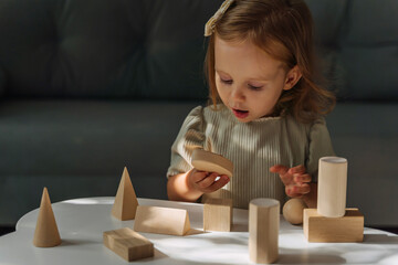 A little girl plays and learns geometric shapes on the table. The kid builds a tower from wooden  blocks. Learning through play. Developing Montessori toddlers activities.