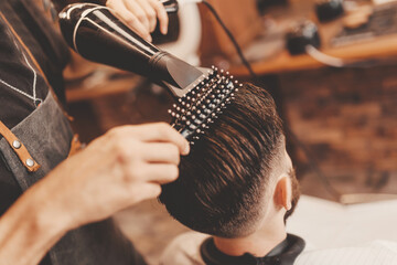 Close-up master Barber does hairstyle and styling with dryer hair to guy. Concept Barbershop...