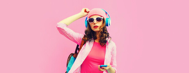 Summer colorful portrait of stylish modern young woman listening to music in headphones with smartphone on pink background, blank copy space for advertising text
