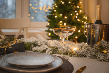 Christmas table setting with elegant empty gray plates decorated gold napkin ring near Xmas tree. Family holiday dinner at home. Close up.