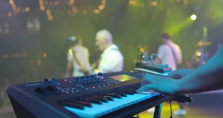 Close up view of musician hand playing synthesizer piano on live concert at stage. The musician playing the electric piano. Music band at background - Powered by Adobe