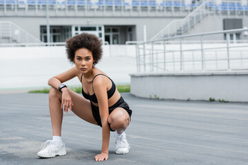Obraz premium African american sportswoman in black sportswear and fitness tracker looking at camera on stadium.