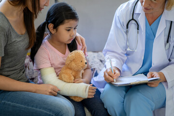 Pediatrician doctor examining little asian girl with a broken arm wearing a cast at hospital - Powered by Adobe