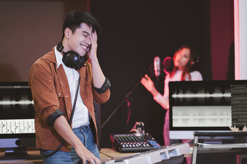 Asian producer standing by sound mixing console. Happy male music composer artist with a woman singer background