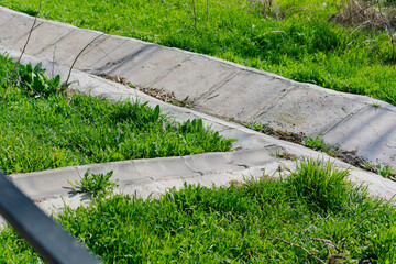 Concrete drain with grass in the garden. Drain channel. Flowing. Meet. Outside. Path. Rain. Stadium. Stream. Tunnel. Way. Channel. Flood. Surface. Basin. Empty