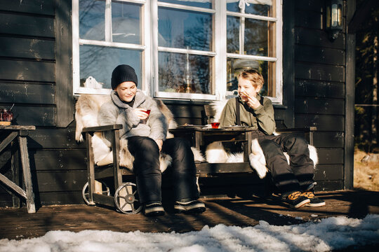 Full length of smiling friends sitting on chairs at porch during winter