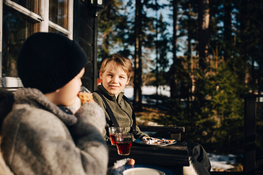 Smiling boy talking with friend while having drink at porch during winter