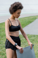 Young african american sportswoman holding fitness mat outdoors.