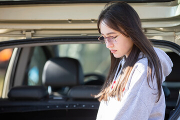 Fototapeta na wymiar A beautiful girl with long hair and glasses on the background of an open car trunk.