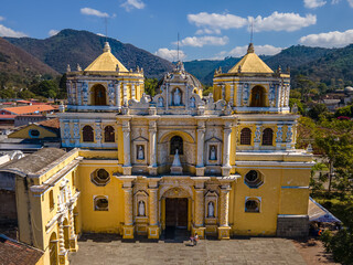 Beautiful aerial cinematic footage of the Antigua City in Guatemala, Its yellow church, the Santa Catalina Arch and the Acatenango Volcano - obrazy, fototapety, plakaty