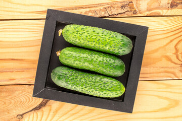 Three ripe green cucumbers with a wooden tray on a wooden table, close-up, top view.