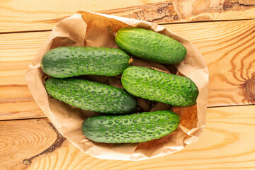Several ripe green cucumbers in a paper bag on a wooden table, close-up, top view.