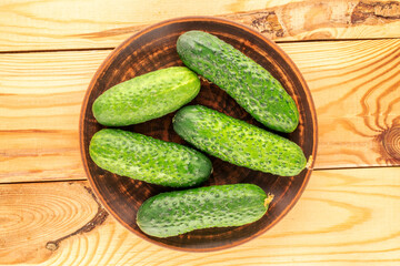 Several ripe green cucumbers with a clay plate on a wooden table, close-up, top view.