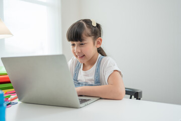 Smiling Asian little girl using laptop doing homework.Child study online on computer at home.