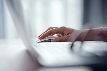 Close up finger of woman using modern white wireless mouse while working on laptop computer on...
