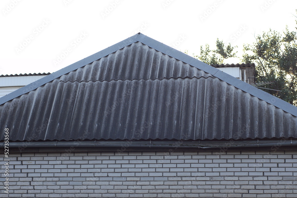 Poster gray slate roof on a white brick private house on the street against the sky