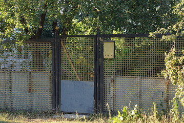 closed door and fence wall made of yellow black metal and iron mesh on the street in green...