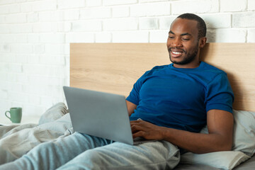 African American Guy Using Laptop Working Online Lying In Bedroom
