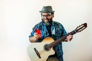 Obraz premium Happy bearded man using smartphone with acoustic guitar.