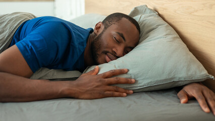 African American Guy Sleeping Peacefully Embracing Pillow Lying In Bedroom