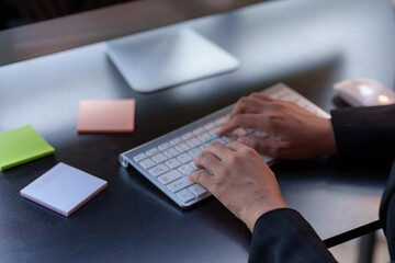 Close-up of a woman's hands sitting intently typing using laptop computer at the office fluently and several documents on the table.