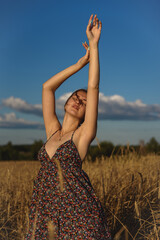 A young girl dances in a wheat field against a blue sky.