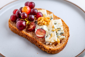 Toasted bread with mild creamy blue cheese, grapes and walnuts on grey plate