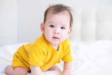 healthy asian baby girl 5 months in yellow bodysuit on bed on white bedding