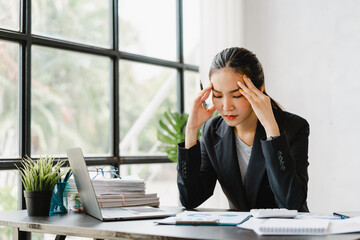 overjoyed young Asian business woman working hard in office feeling headache at desk in office.