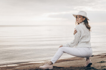 blonde girl in a white hat walks along the seashore on an autumn day - 527368100