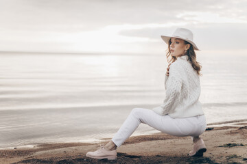 blonde girl in a white hat walks along the seashore on an autumn day - 527368102