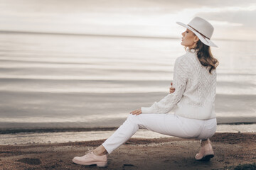 blonde girl in a white hat walks along the seashore on an autumn day - 527368103