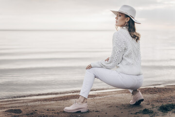 blonde girl in a white hat walks along the seashore on an autumn day - 527368104